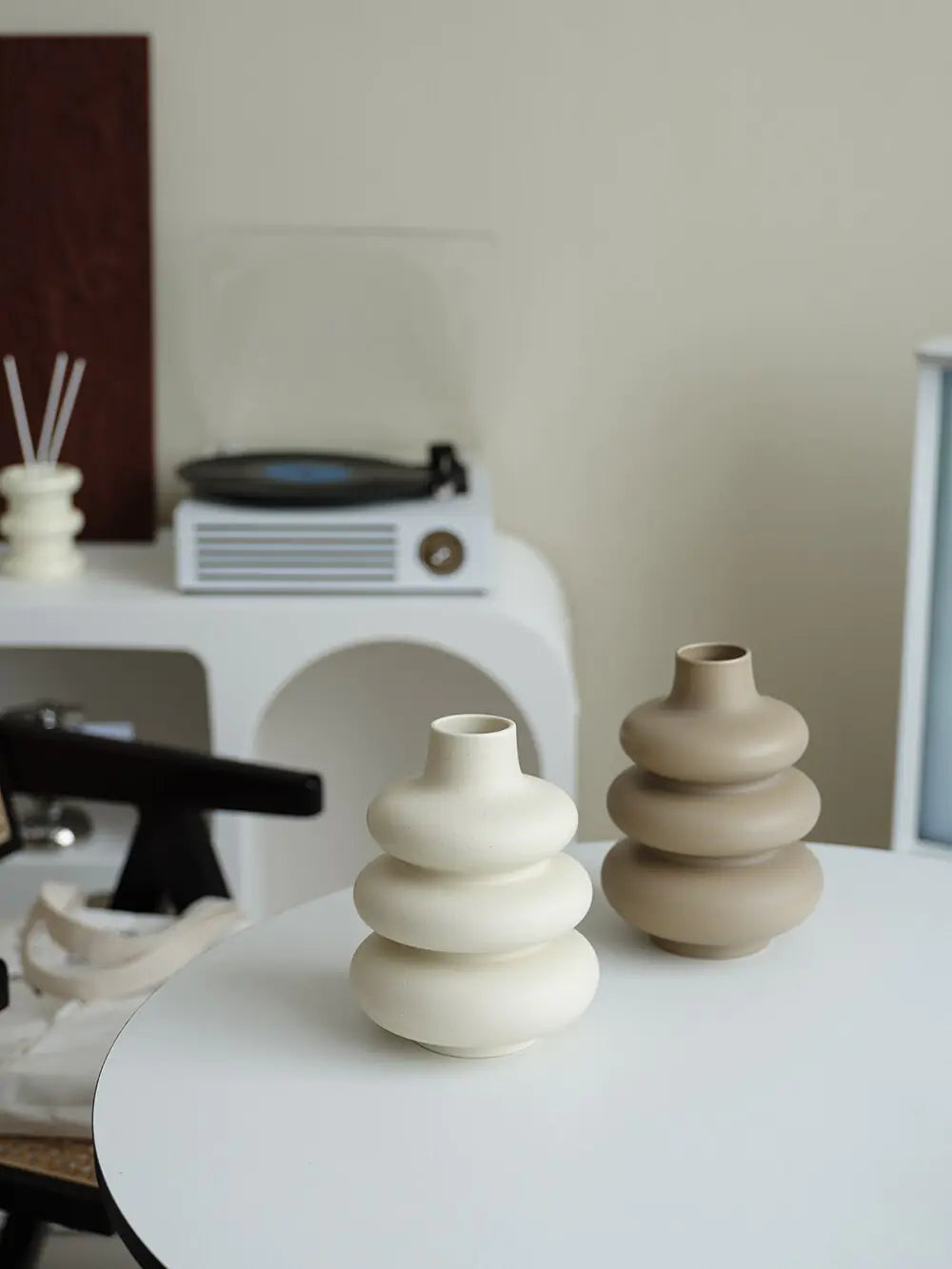 Two large ceramic vases in neutral tones with donut-shaped layers on a white table in a modern room