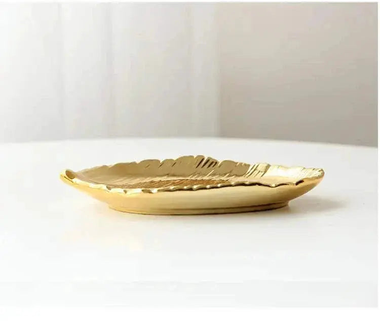 Gold ceramic jewelry tray with leaf design on white surface