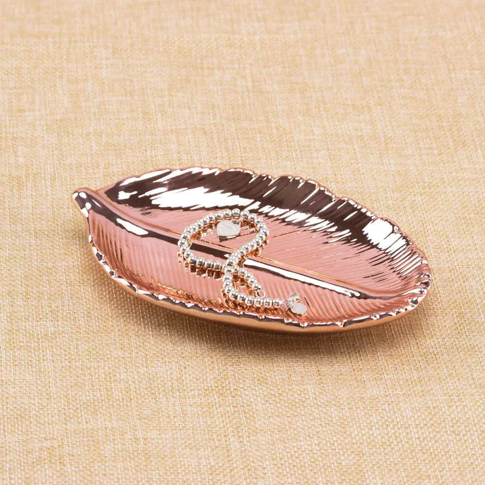 Rose gold ceramic jewelry tray shaped like a leaf with gold electroplated finish on beige fabric background