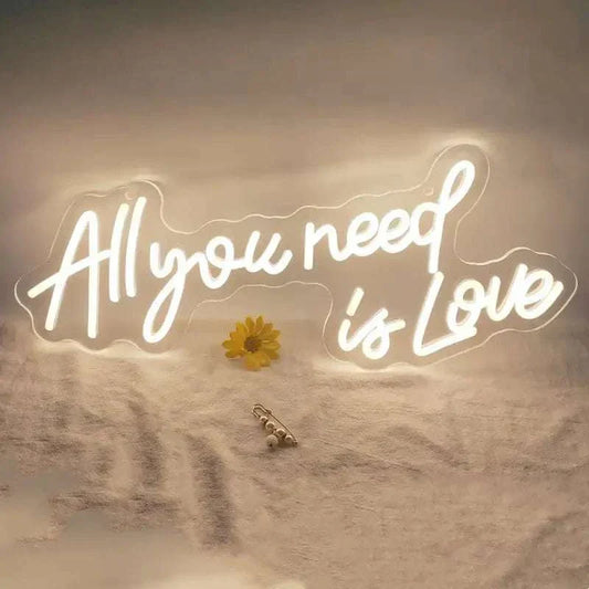 White LED neon sign spelling "All you need is Love" with warm glow on a soft fabric background