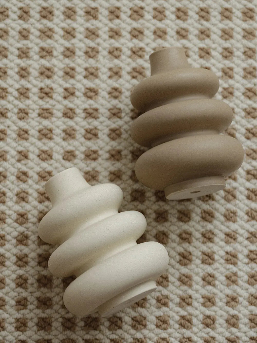 Two large ceramic vases in donut shapes with a matte finish on a textured beige surface