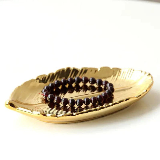 Gold ceramic jewelry tray with leaf design holding a dark beaded bracelet