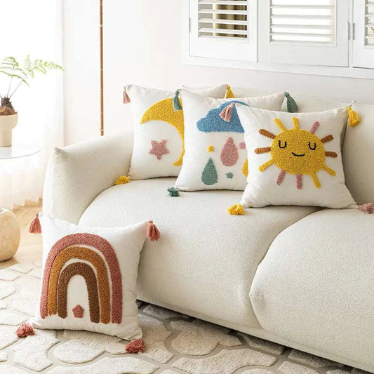 Set of tufted loop pillow covers featuring sun, moon, rainbow, and abstract designs on a white sofa with tassels at corners
