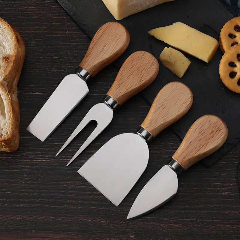 Cheese knife set with stainless steel blades and oak handles on dark wooden surface with cheese and bread pieces.