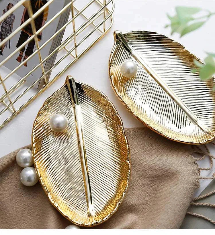 Gold ceramic jewelry trays shaped like leaves with pearl accents on a beige cloth.