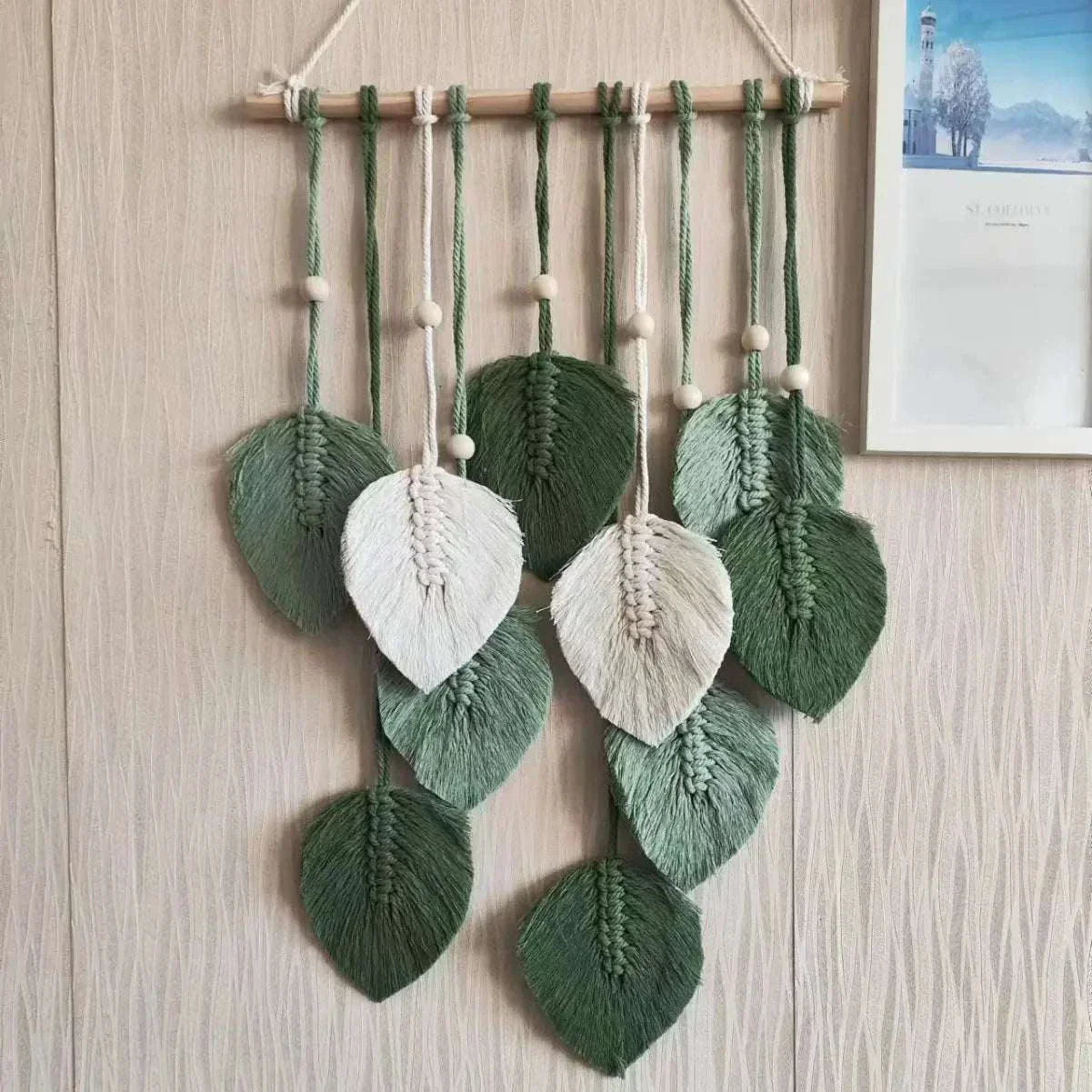 Handmade woven tapestry with green and white leaf designs hanging on wooden rod for bohemian wall decor
