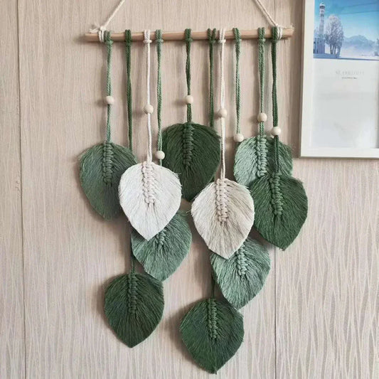 Handmade woven tapestry with green and white leaf designs hanging on wooden rod for bohemian wall decor