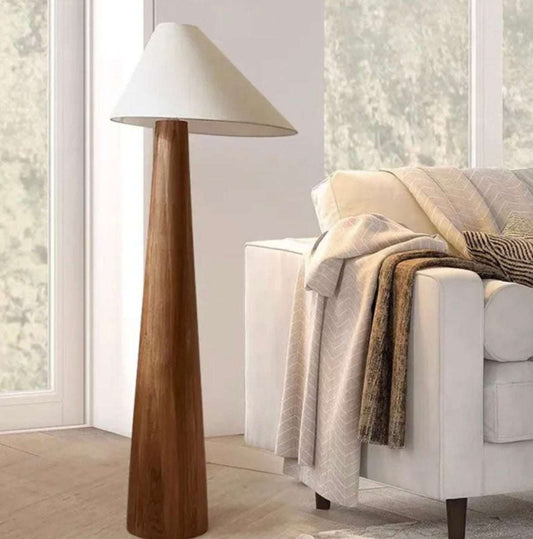 Wabi-sabi solid wood floor lamp with a minimalist wooden base and white conical shade beside a cozy sofa.