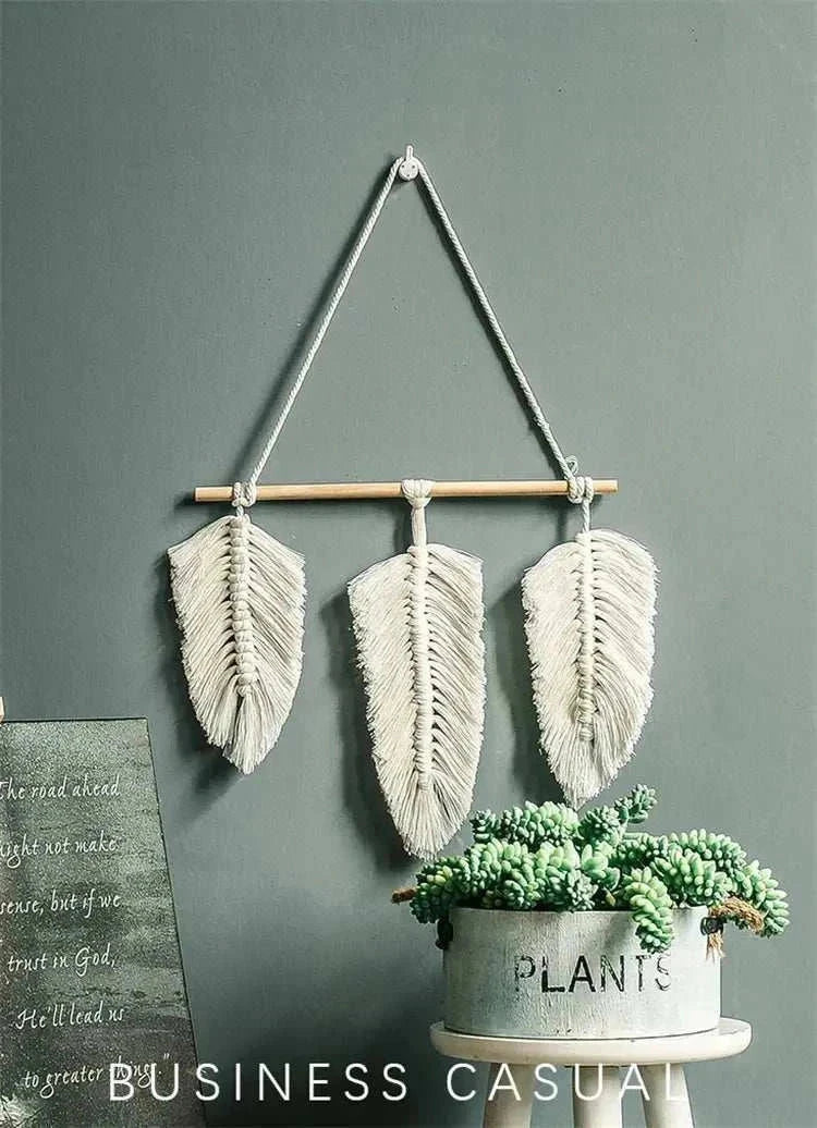 Bohemian woven leaf wall hanging in natural beige cotton with three detailed leaves, hanging above a succulent plant pot.
