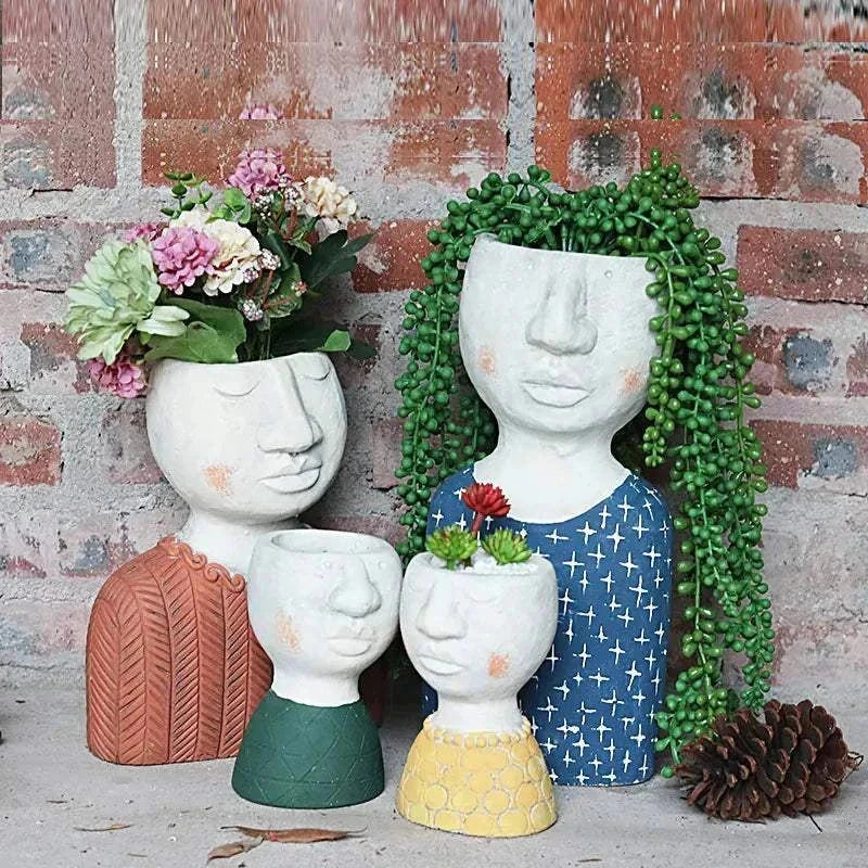 Set of four artistic portrait sculpture planters with plants, featuring unique face designs and colorful clothing details against a brick wall background.