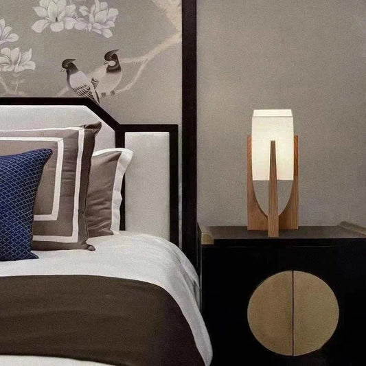 Bedroom bedside wooden decorative table lamp with fabric shade on a black nightstand next to a bed with white and brown bedding.