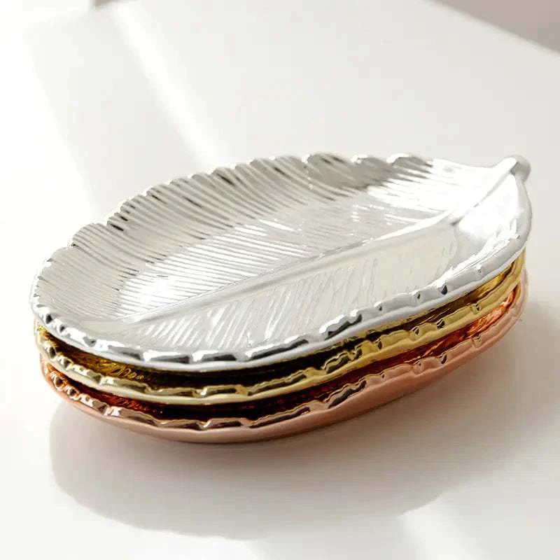 Stacked ceramic jewelry trays in silver, gold, and rose gold with a gold leaf design and electroplated finish.