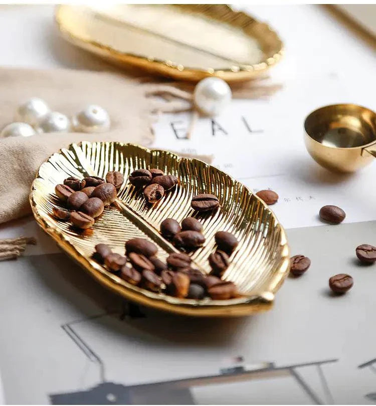 Gold ceramic jewelry tray with leaf design holding coffee beans on table surface