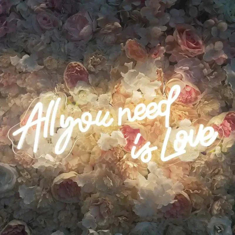 LED neon sign glowing warm white with "All you need is Love" text on floral background wall decor