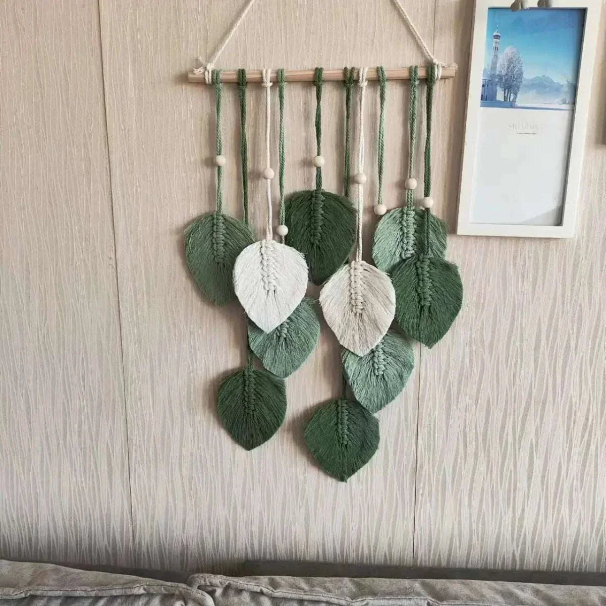 Handmade woven tapestry wall decor featuring green and white leaf designs with fringe detailing in a bohemian style