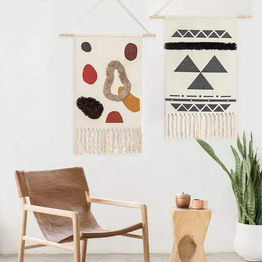 Handcrafted woven tapestry wall hangings with geometric and abstract designs, featuring tassels, displayed in a cozy living space with a wooden chair and plant.