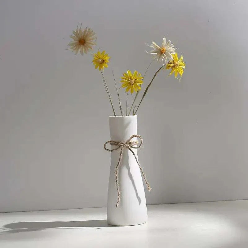 White hemp rope ceramic vase with minimalist design holding yellow and white flowers on a white surface